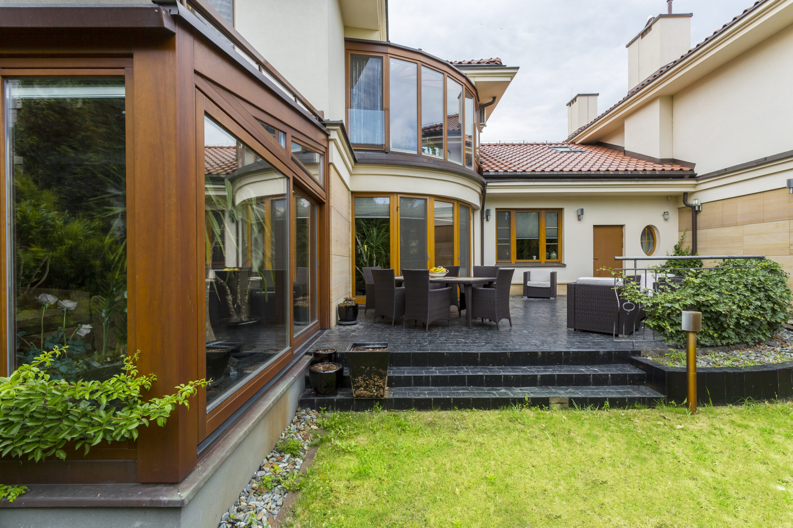 Elegant terrace with garden furniture in the backyard of villa with many windows